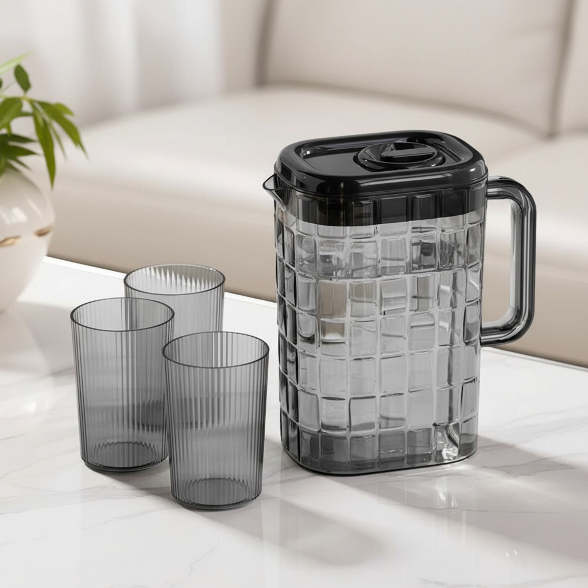 Black and transparent glass pitcher with three matching glasses on a light surface.