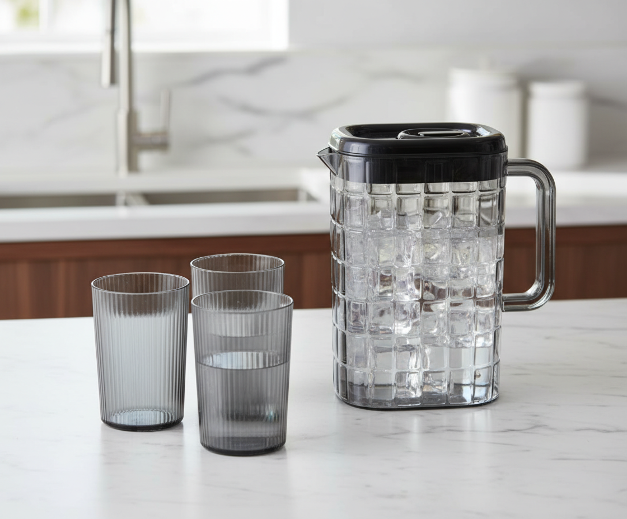 Clear pitcher with ice and three glasses on a kitchen counter