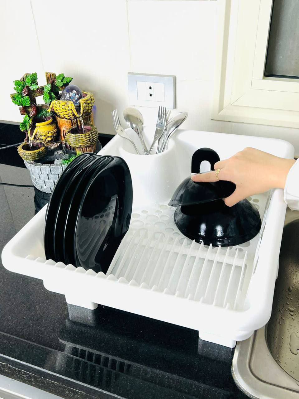 White dish drainer with black dishes on a kitchen counter