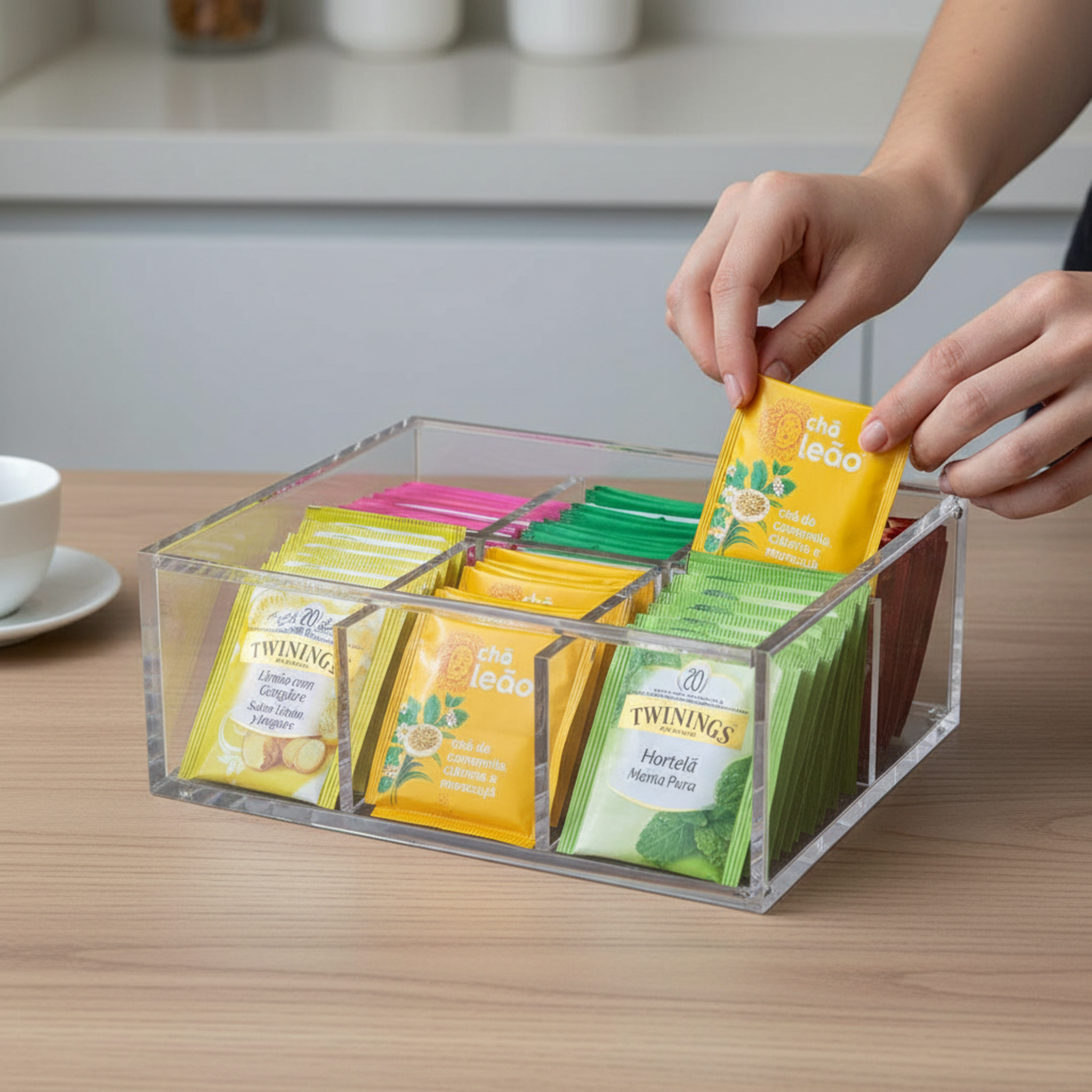 Person selecting a Twinings tea bag from an acrylic organizer on a kitchen counter.
