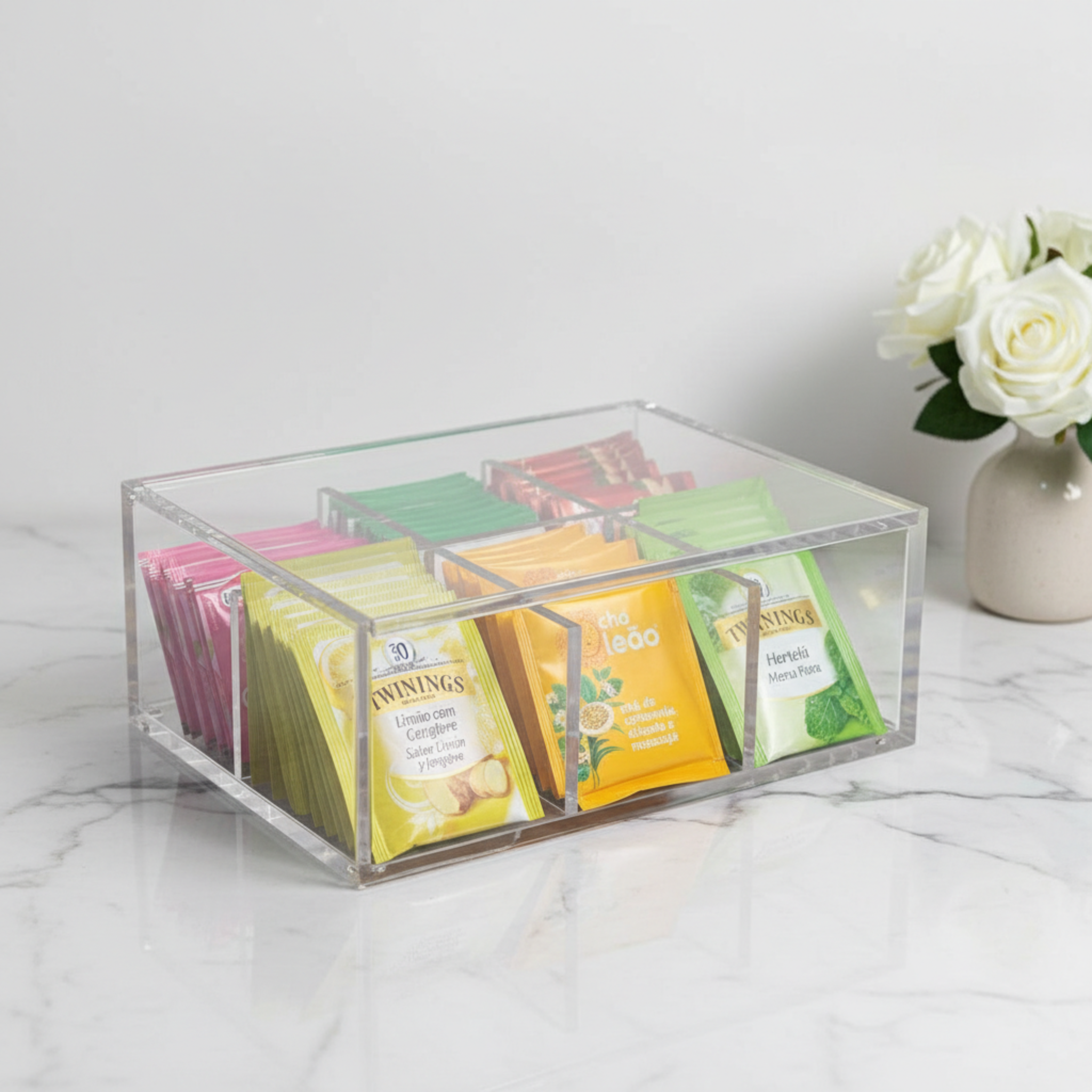 Clear acrylic tea bag organizer with assorted tea bags on a marble surface.