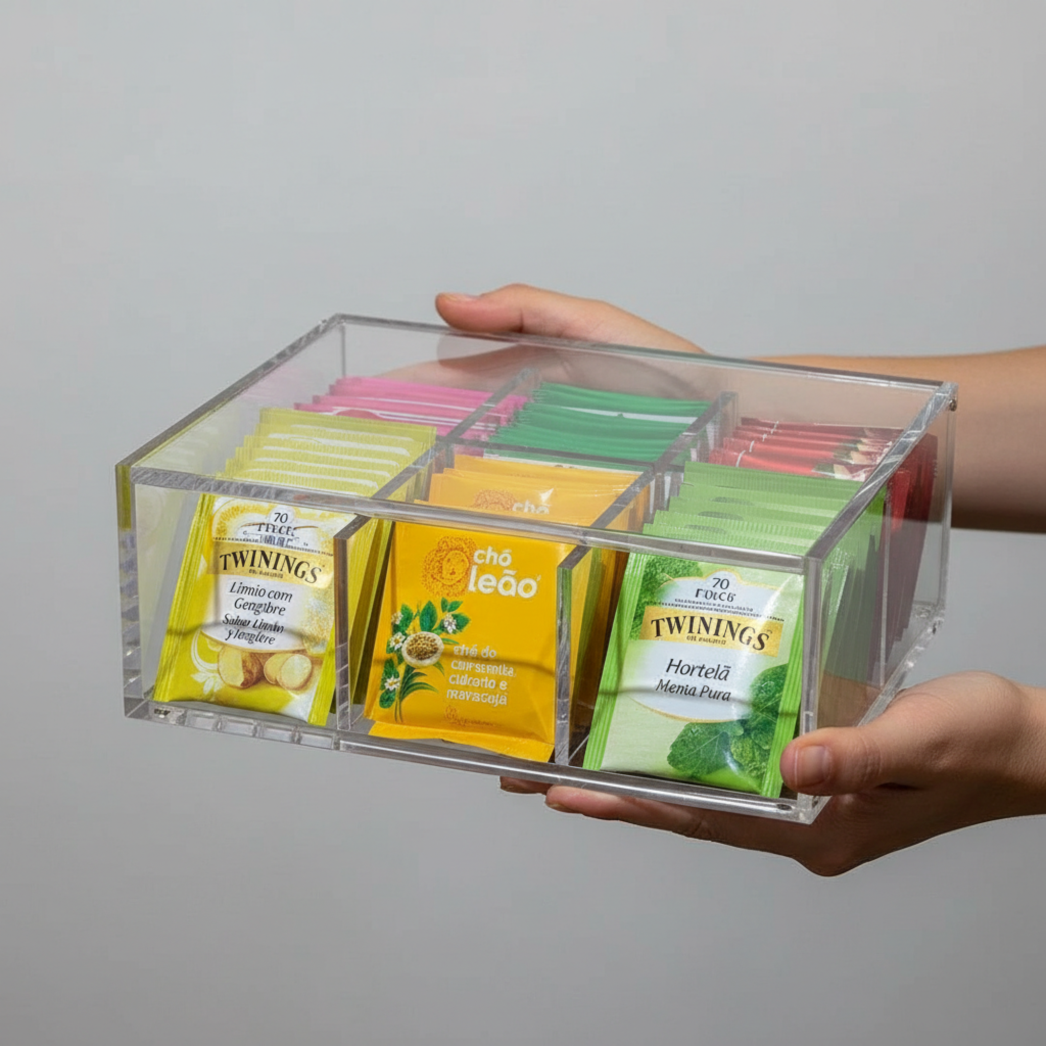 Clear organizer with assorted tea bags including Twinings, held by a person against a gray background