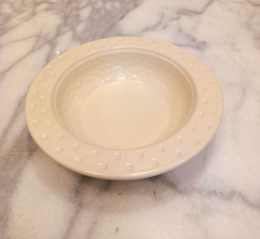 Offwhite ceramic bowl with textured rim on a marble surface